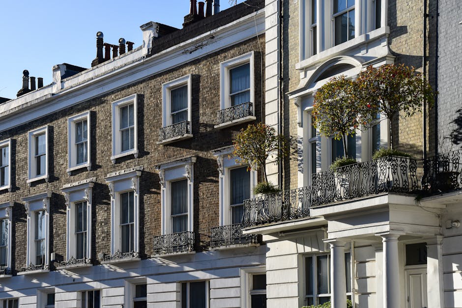 A row of multi-storey Victorian-style residential buildings with brick facades, each featuring large sash windows, decorative white trim, and small wrought iron balconies. The image shows the exterior
