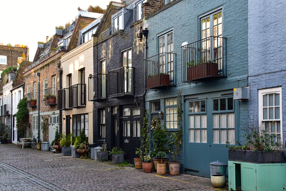 A row of multi-storey Victorian-style residential buildings with brick facades, each featuring large sash windows, decorative white trim, and small wrought iron balconies. The image shows the exterior