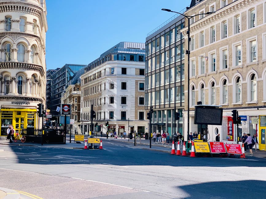 A busy street scene on Shaftesbury Avenue in Soho, featuring narrow pavements lined with multi-story retail and residential buildings with traditional architectural details, including large windows an